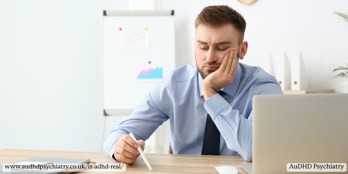 : Frustrated adult male holding his head at a desk, representing undiagnosed ADHD in the workplace