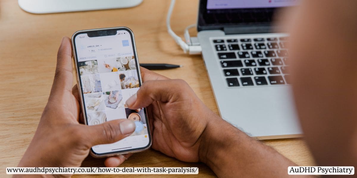 Person scrolling on phone while laptop is open, symbolising ADHD scrolling paralysis