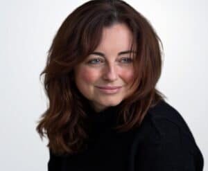 A woman with shoulder-length brown hair and a black top smiling gently, representing professional mental health support for AuDHD and psychiatric services.