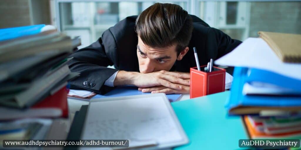 Man lying on desk with stacks of papers – exhaustion from ADHD burnout