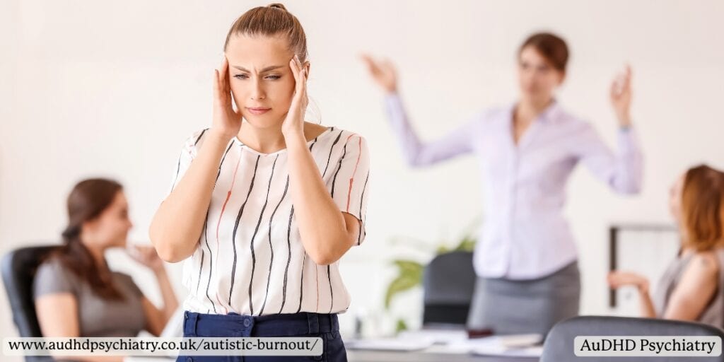 Woman covering her ears at noisy office – sensory overload during autistic burnout